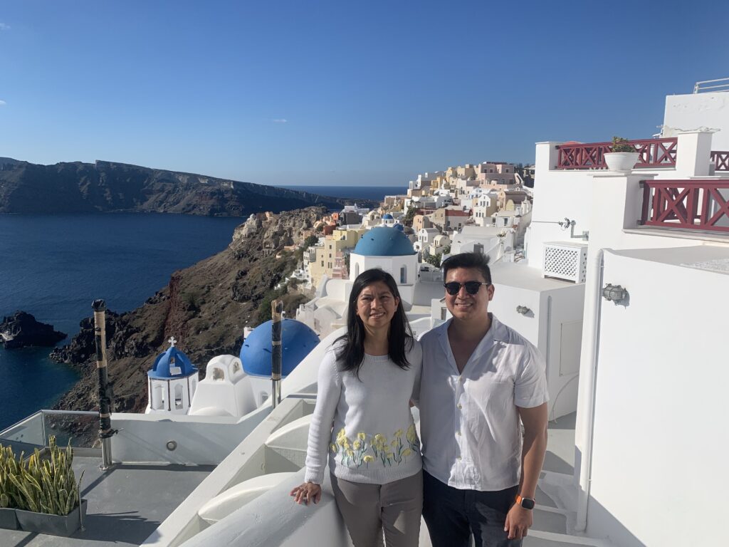 A lady and man standing in front of the three blue domes in Oia Village