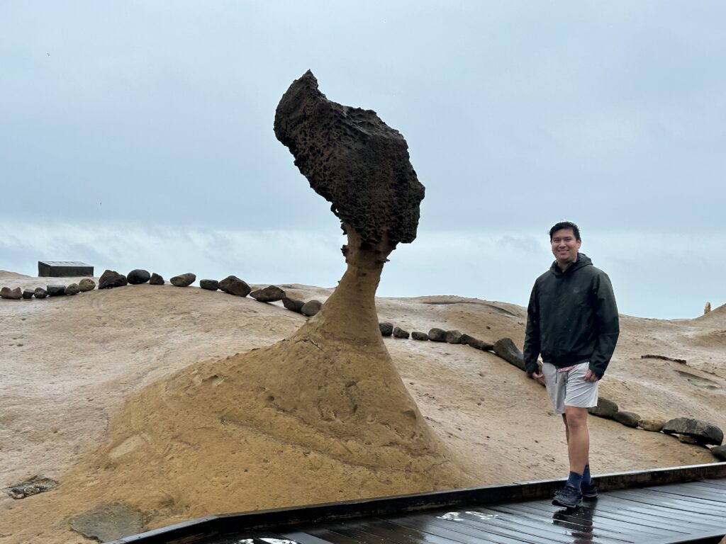 A man in a rain jacket posing with a rock in the shape of a queens head